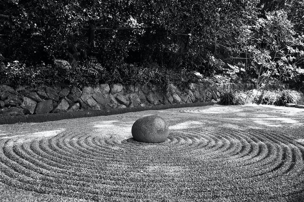 Schwarz-weiß Bild eines Zen Garten mit im vielen kleinen Steinkiesel, die Kreise bilden. In der Mitte befindet sich ein Steinblock.